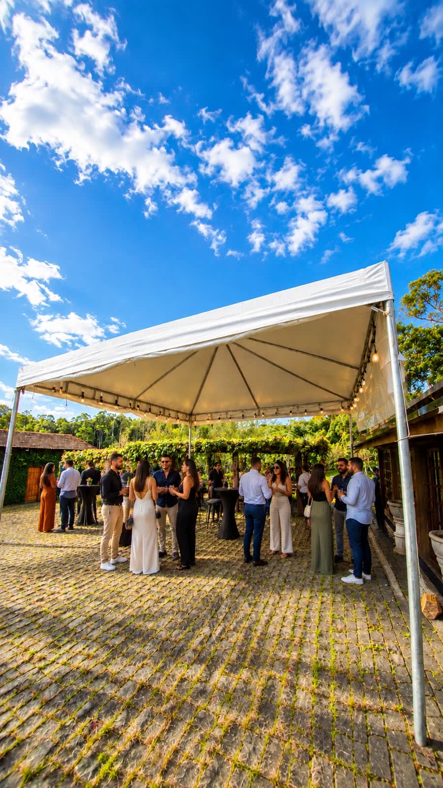 Convidados reunidos sob tenda branca com varal de lâmpadas